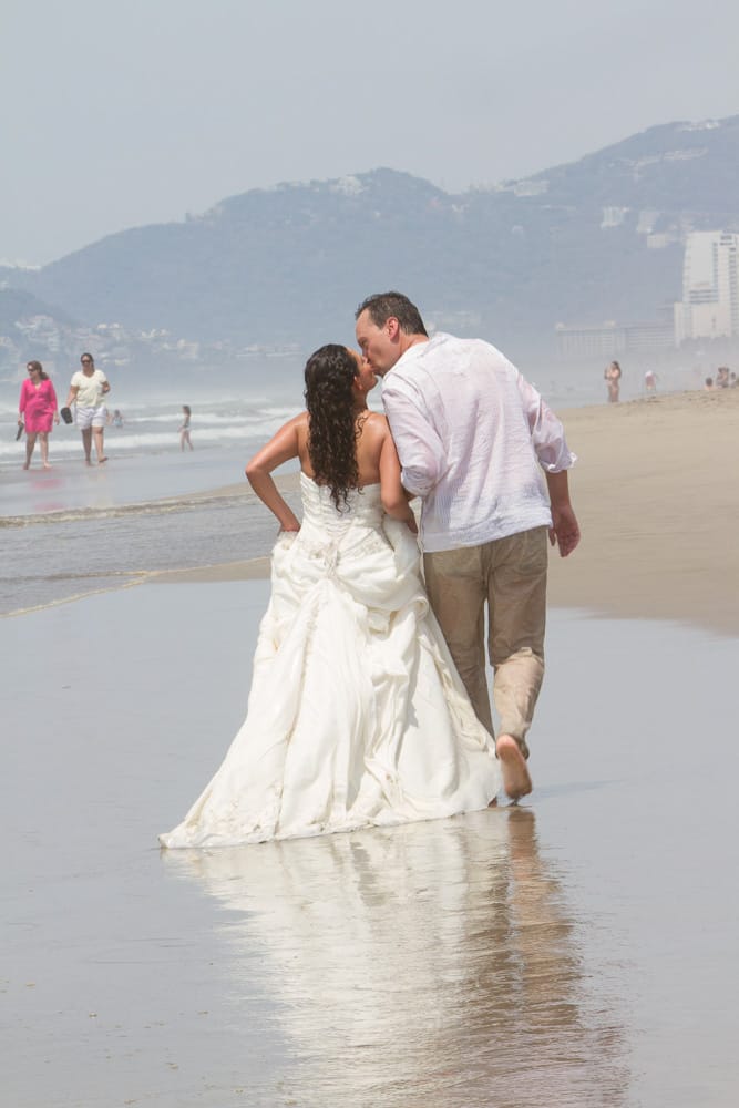 Una novia y un novio besándose en la playa.