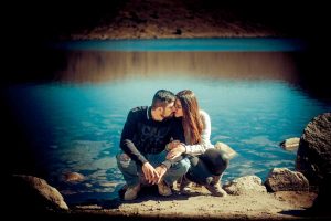 una pareja está sentada en las rocas cerca de un lago.